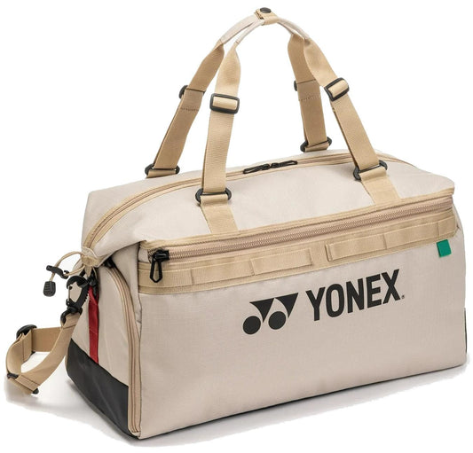 The Yonex BA72611EX Gearlogic Tennis Boston Bag in beige features tan straps, black logo and text, side compartments, black and red accents, zippered closures, a rectangular shape, and is made from recycled polyester.