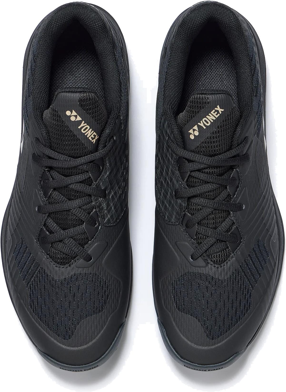 A pair of Yonex Power Cushion Sonicage Men’s Tennis Shoes in Black/Mocha Grey, viewed from above, featuring mesh uppers, black laces, textured details, and gold Yonex logos on the tongues for a lightweight tennis experience.