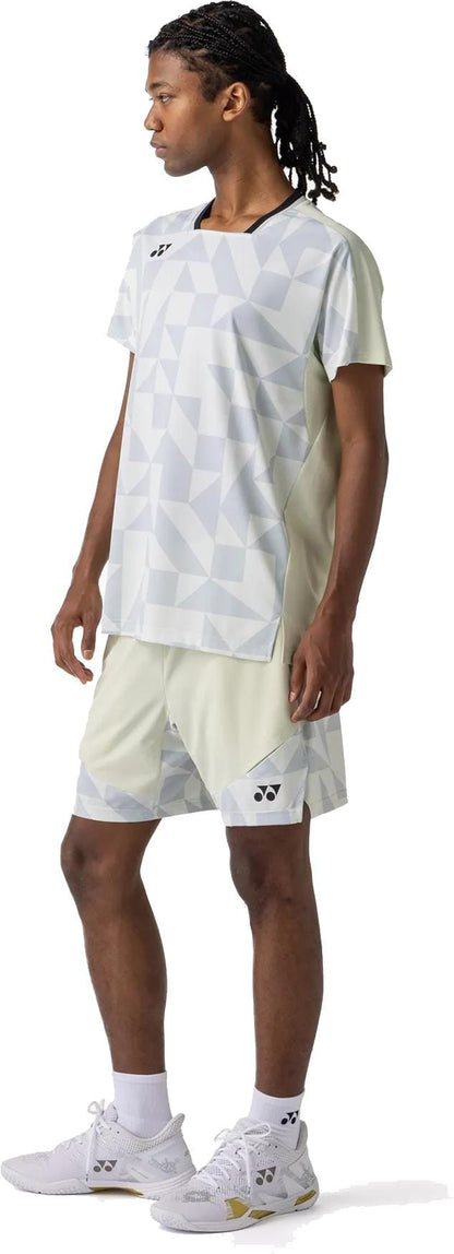 A person with braided hair stands sideways, wearing the Yonex 10712YX Crew Neck Men's Tennis T-Shirt in Champagne, paired with matching shorts, white socks, and white athletic shoes against a plain white background.