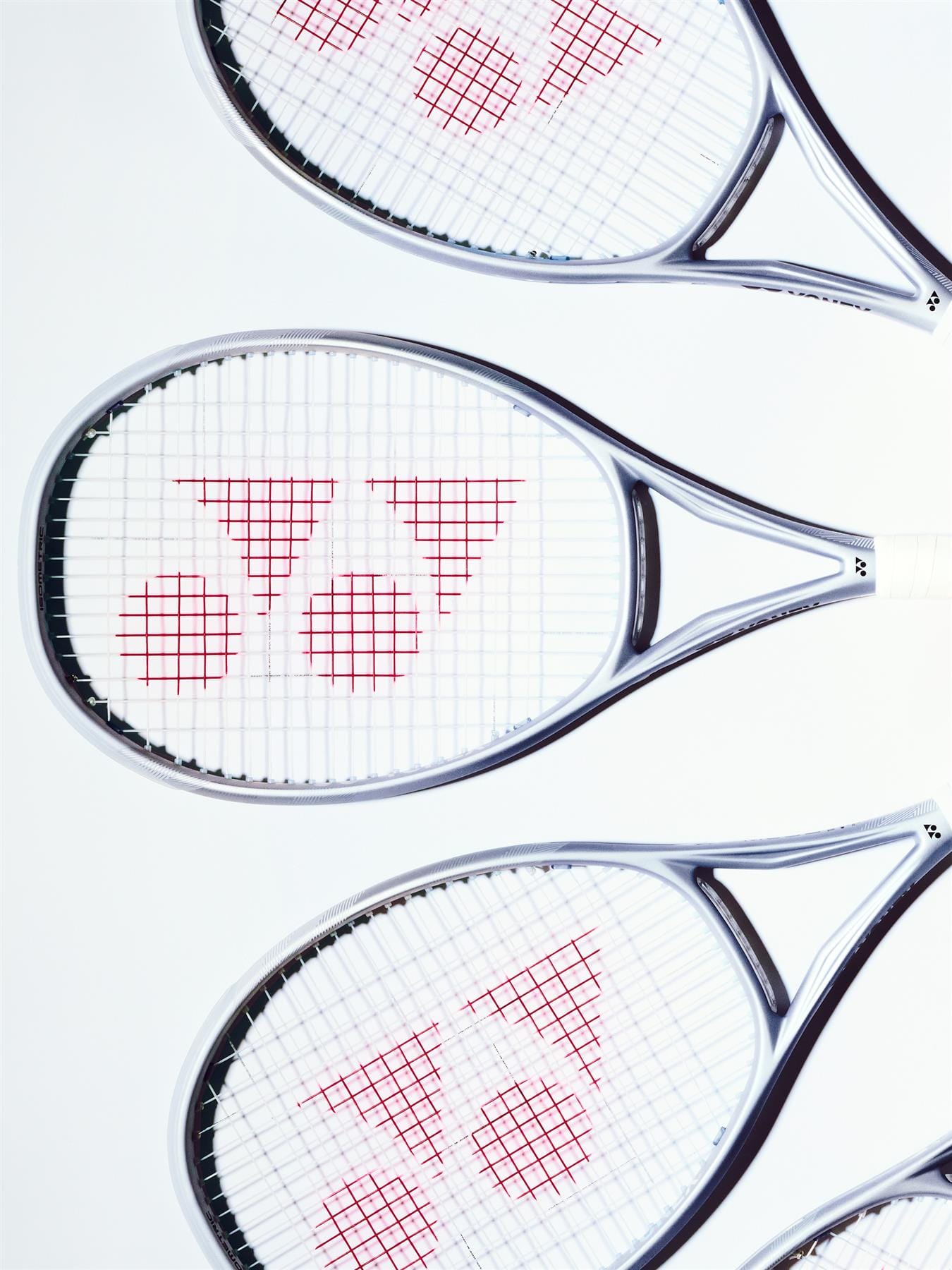 Three Yonex Muse 100L Tennis Rackets by Yonex, featuring white frames and red geometric string patterns, are arranged diagonally on a light background to showcase their Synchro Frame for effortless rallies.