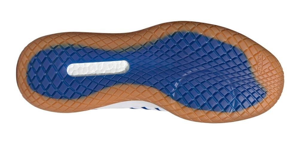 The image displays the sole of an adidas Stabil Next Gen Primeblue men's indoor shoe in Cloud White and Core Black, featuring a geometric pattern. The outer edge is brown, the central area is blue with a white section in the middle, designed to provide energy return while maintaining traction and style.