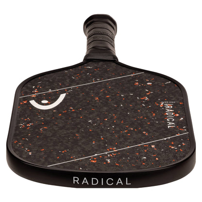 A close-up view of the HEAD Radical Pro EX15 2026 Pickleball Paddle, featuring orange and white specks, the word "RADICAL" on both the handle and face, a raw carbon surface, and a textured grip.