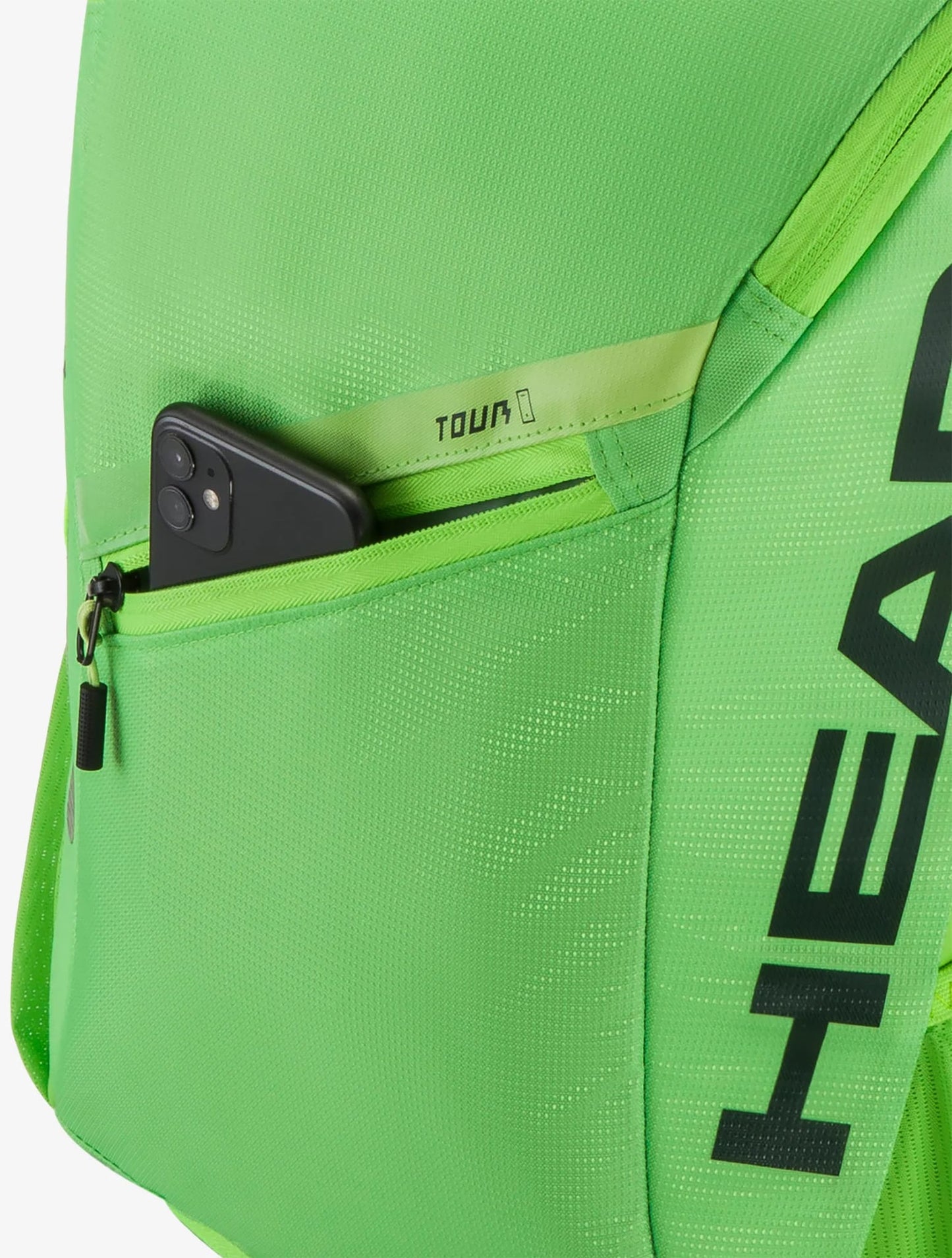 A black smartphone is partially visible in the zippered pocket of a bright green HEAD Tour 25L Tennis Backpack - Sharp Green, with the word "TOUR" printed near the zipper.