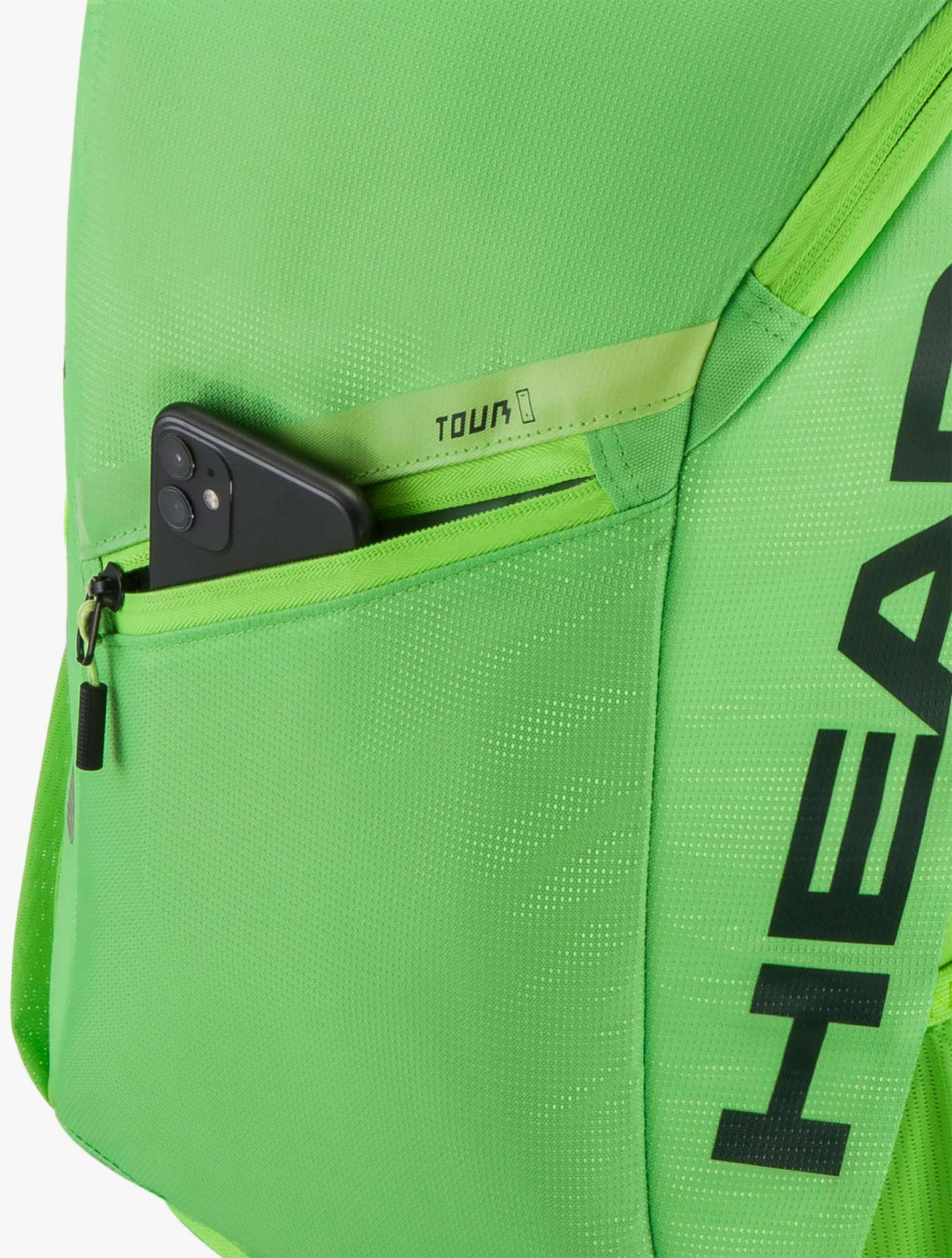 A black smartphone is partially visible in the zippered pocket of a bright green HEAD Tour 25L Tennis Backpack - Sharp Green, with the word "TOUR" printed near the zipper.