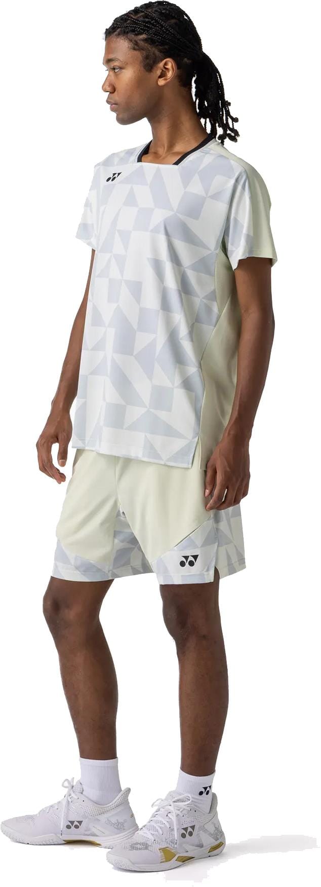 A person stands sideways in a light geometric-patterned sports outfit featuring Yonex 15240YX Knit Men's Tennis Shorts in Champagne, a matching T-shirt, white socks, and athletic shoes against a plain white background.