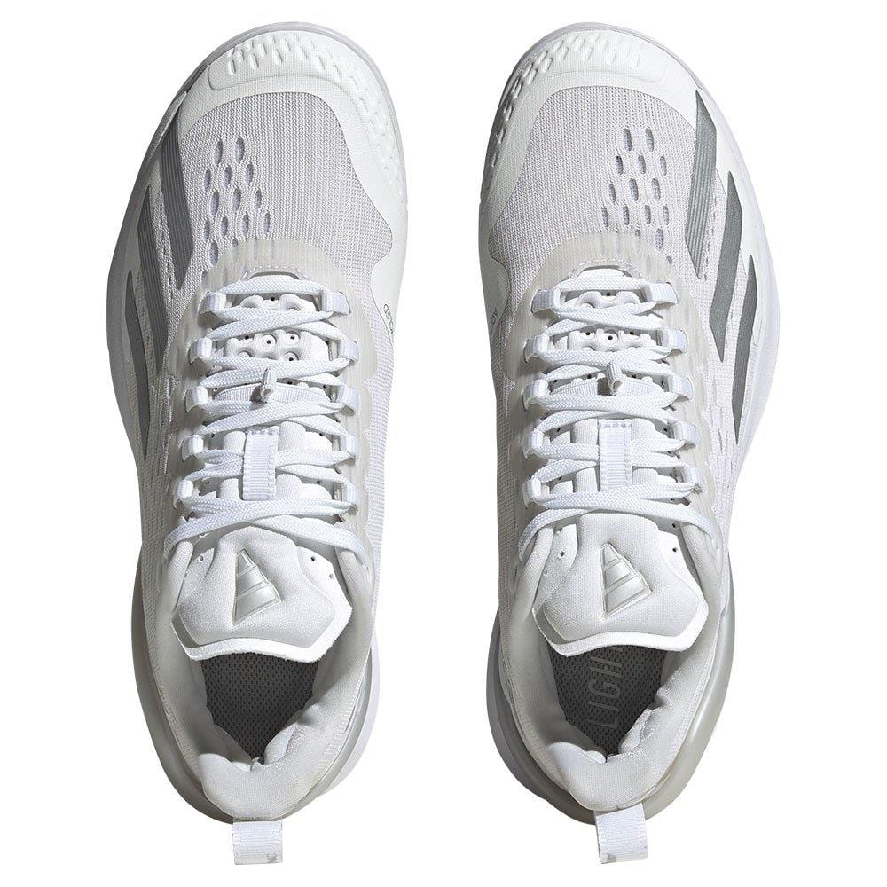 A top-down shot reveals a pair of women's tennis shoes in white, accented with silver, characterized by mesh uppers and unique stripe designs on the sides. These Adidas Adizero Cybersonic sneakers are equipped with lace-up closures and cushioned soles for enhanced comfort, style, and swift movement.