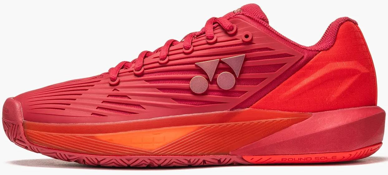 The Yonex Power Cushion Eclipsion 5 Mens Tennis Shoes in Ruby Red feature textured detailing, lace-up closure, a double-dot logo, subtle orange outsole accents, "ROUND SOLE" branding by the heel, and Yonex’s signature cushioning technology.