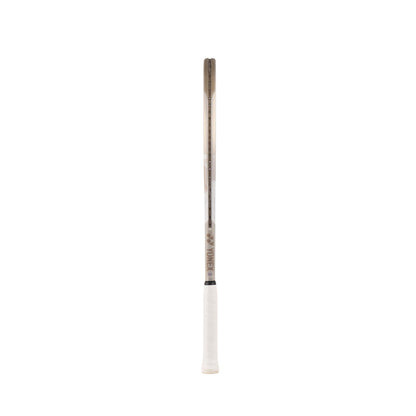 The Yonex VCORE Game Tennis Racket in Sand Beige stands against a plain white backdrop, featuring a white grip and brownish frame. Its design reflects the innovative style of VCORE rackets, combining classic aesthetics with modern performance, with "Yonex" on the side.