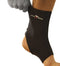 A person wearing a black Precision Neoprene Ankle Support from the Precision brand demonstrates how the support aids in recovering from minor sprains. The ankle support effectively covers the ankle, providing necessary support while the individual holds their lower leg to showcase its usefulness.