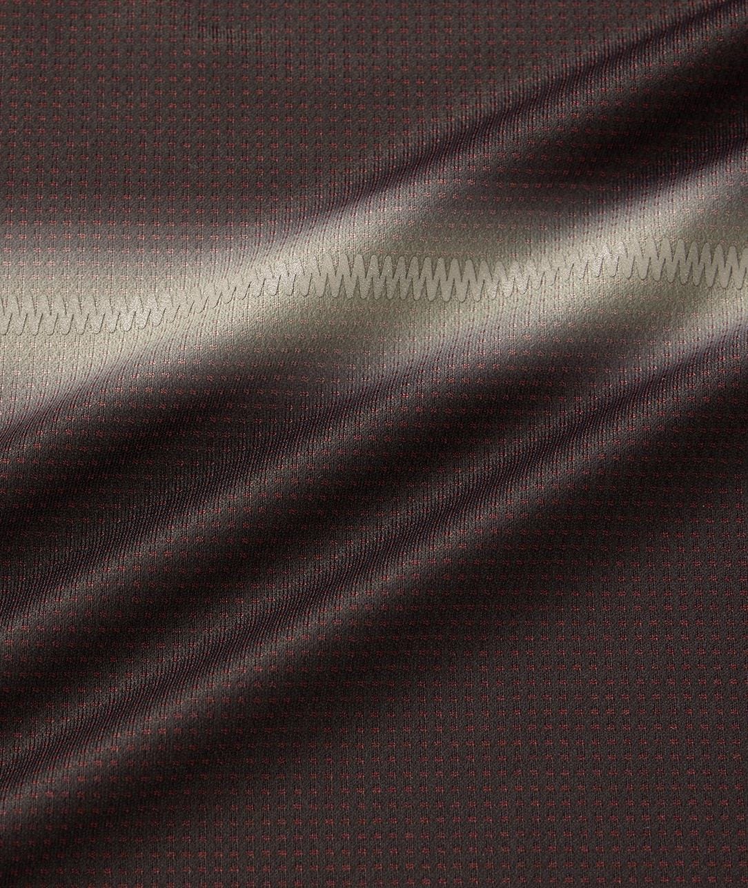 Close-up of black fabric with subtle red dots from the Yonex 10711YX Crew Neck Mens Tennis T-Shirt; a zigzag seam runs horizontally, and soft light highlights the moisture-wicking texture and gentle folds.