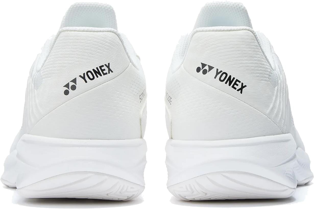 Two white Yonex Power Cushion Sonicage Wide Unisex Tennis Shoes are shown from the back, featuring the Yonex logo and name in black on the heels. These lightweight shoes have textured soles and a sleek, clean look.