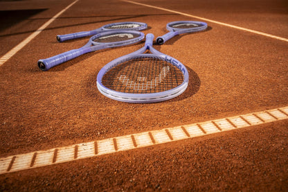 Four HEAD tennis rackets, including the HEAD Boom MP L Alternate 2026 Tennis Racket, lie near the baseline on the clay court. Distinct white lines highlight both power and touch on the reddish-brown surface.