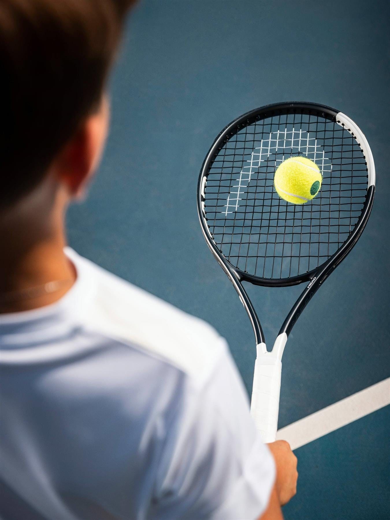 A person in a white shirt holds the HEAD Speed Junior 25 2026 Tennis Racket as a yellow tennis ball hovers above its strings on a blue court.