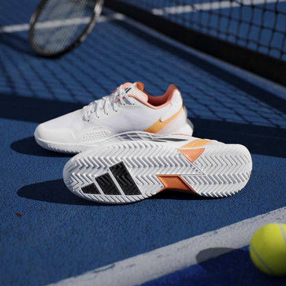 The adidas ADIDAS Defiant Speed 2 Men's Tennis Shoes in White/Orange are shown on a blue tennis court with a racket and yellow ball by the net, highlighting these lightweight men's shoes from adidas.