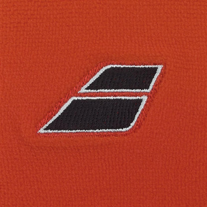 Close-up of two Babolat Terry Jumbo Wristbands in Cherry Tomato, featuring a black parallelogram shape with white borders, stitched onto orange textured fabric. The large wristbands slightly overlap and angle to the right.