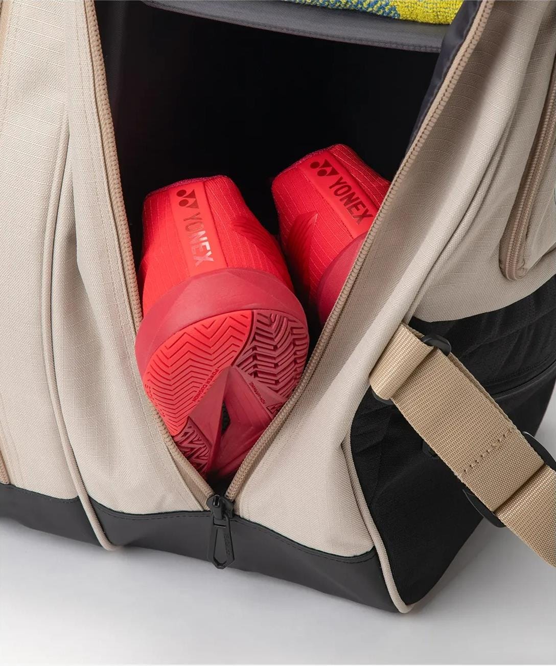 A pair of bright red Yonex sports shoes is stored in a partially unzipped Yonex BA72626EX Gearlogic 6 Racket Tennis Bag in beige, crafted from recycled polyester for eco-friendly style.