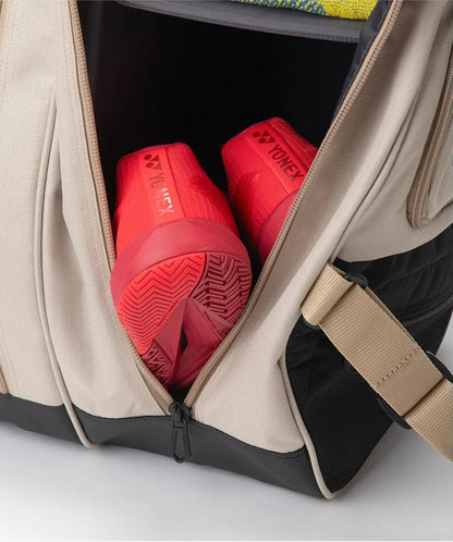 A pair of bright red Yonex sports shoes is stored in a partially unzipped Yonex BA72626EX Gearlogic 6 Racket Tennis Bag in beige, crafted from recycled polyester for eco-friendly style.