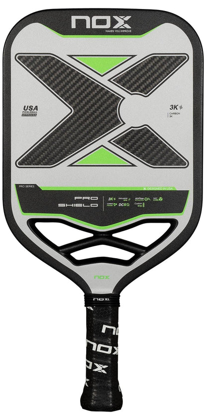 The NOX NOV Pro Shield Pickleball Paddle in black and green features a large "X" design, textured Spin Technology carbon fiber face, “Pro Series” and “Pro Shield” labeling, plus a black grip with NOX branding.