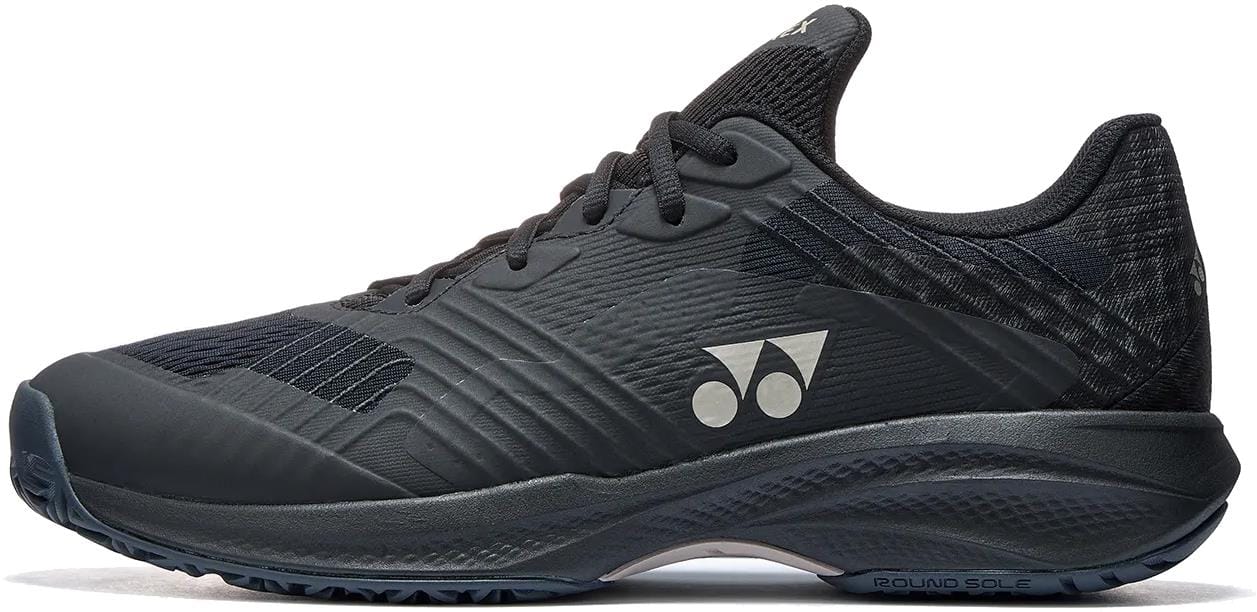 The Yonex Power Cushion Sonicage Men's Tennis Shoes in Black/Mocha Grey feature textured details, laces, a low-profile design, two white circular side logos, and a patterned sole—perfect for sports or casual wear.