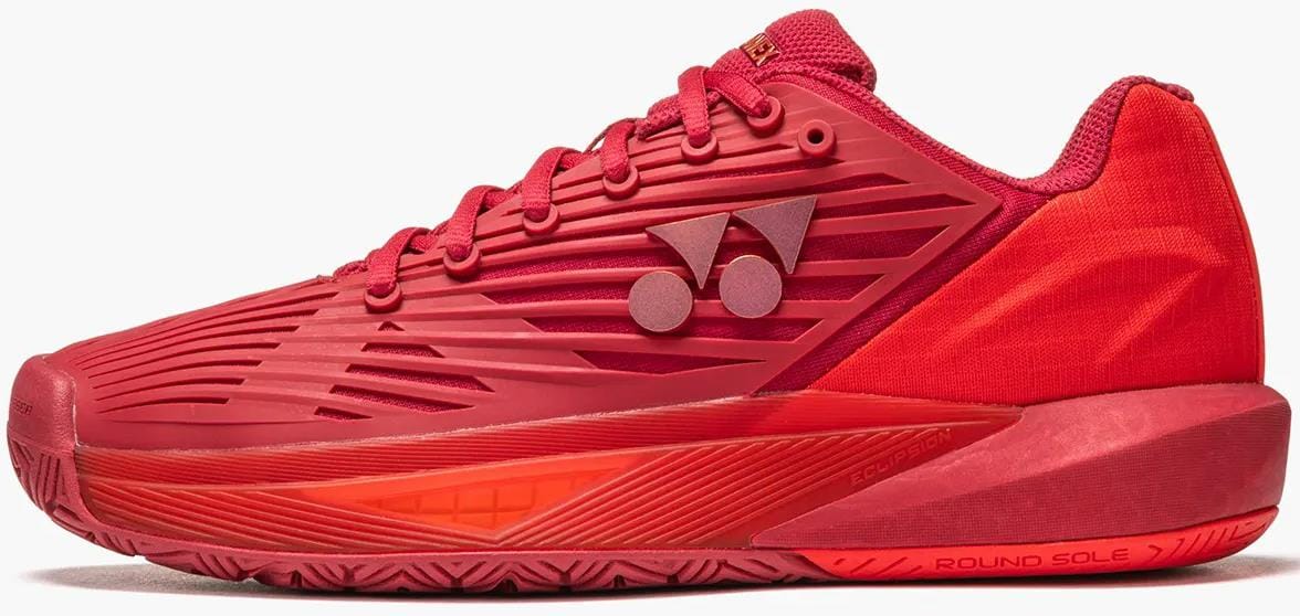 The Yonex Power Cushion Eclipsion 5 Women's Tennis Shoes in Ruby Red feature a textured design, lace-up closure, geometric side patterns, a round sole, and the Yonex logo near the ankle.