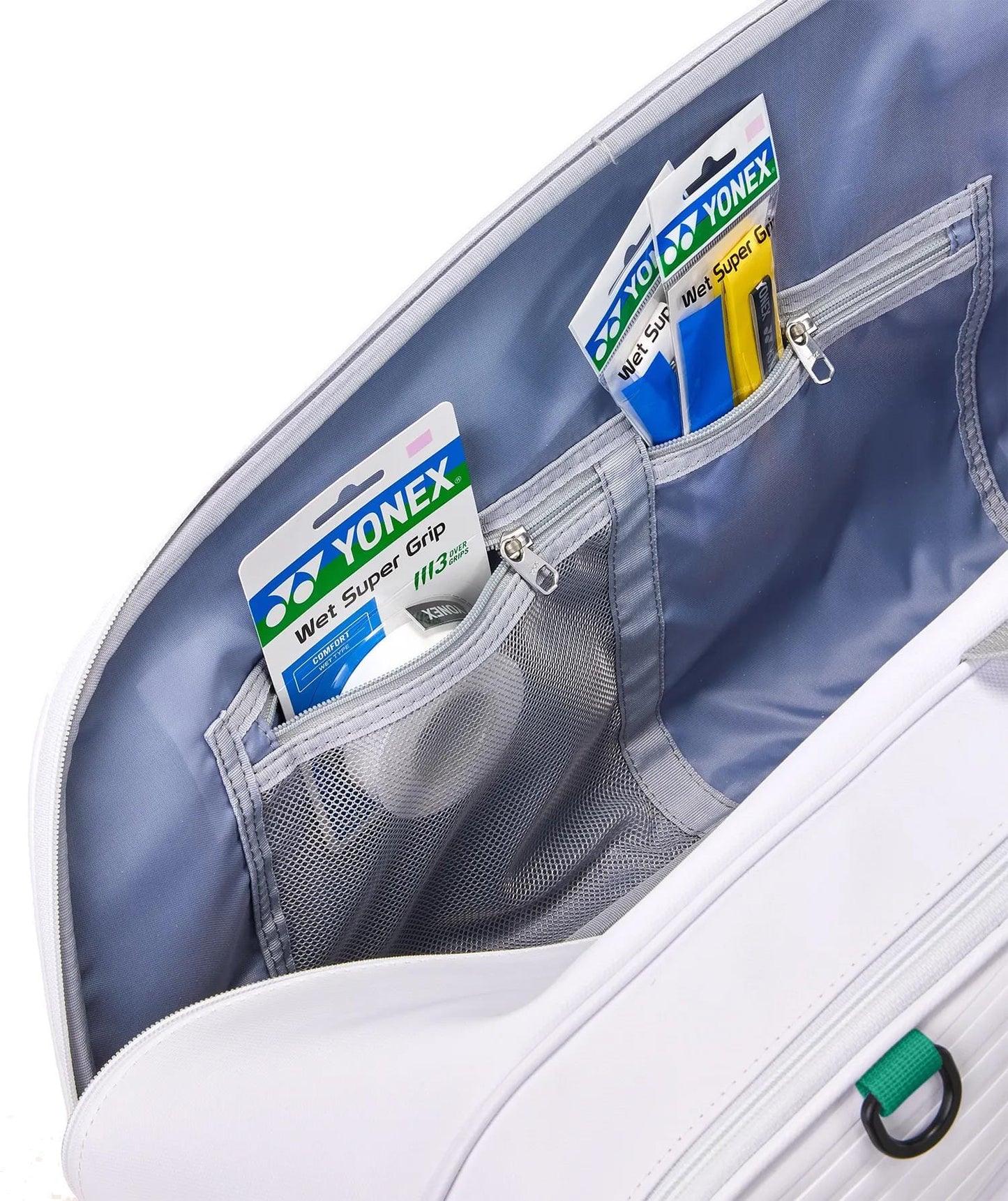 The Yonex 02626EX Expert 6 Racket Tennis Bag in white is open, revealing mesh and zippered interior pockets with Yonex Wet Super Grip badminton grips in their packaging stored inside.