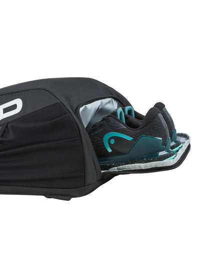 A close-up of the HEAD Tour 25L Tennis Backpack - Black by HEAD, showing its partially unzipped ventilated compartment with a pair of black and teal athletic shoes inside.