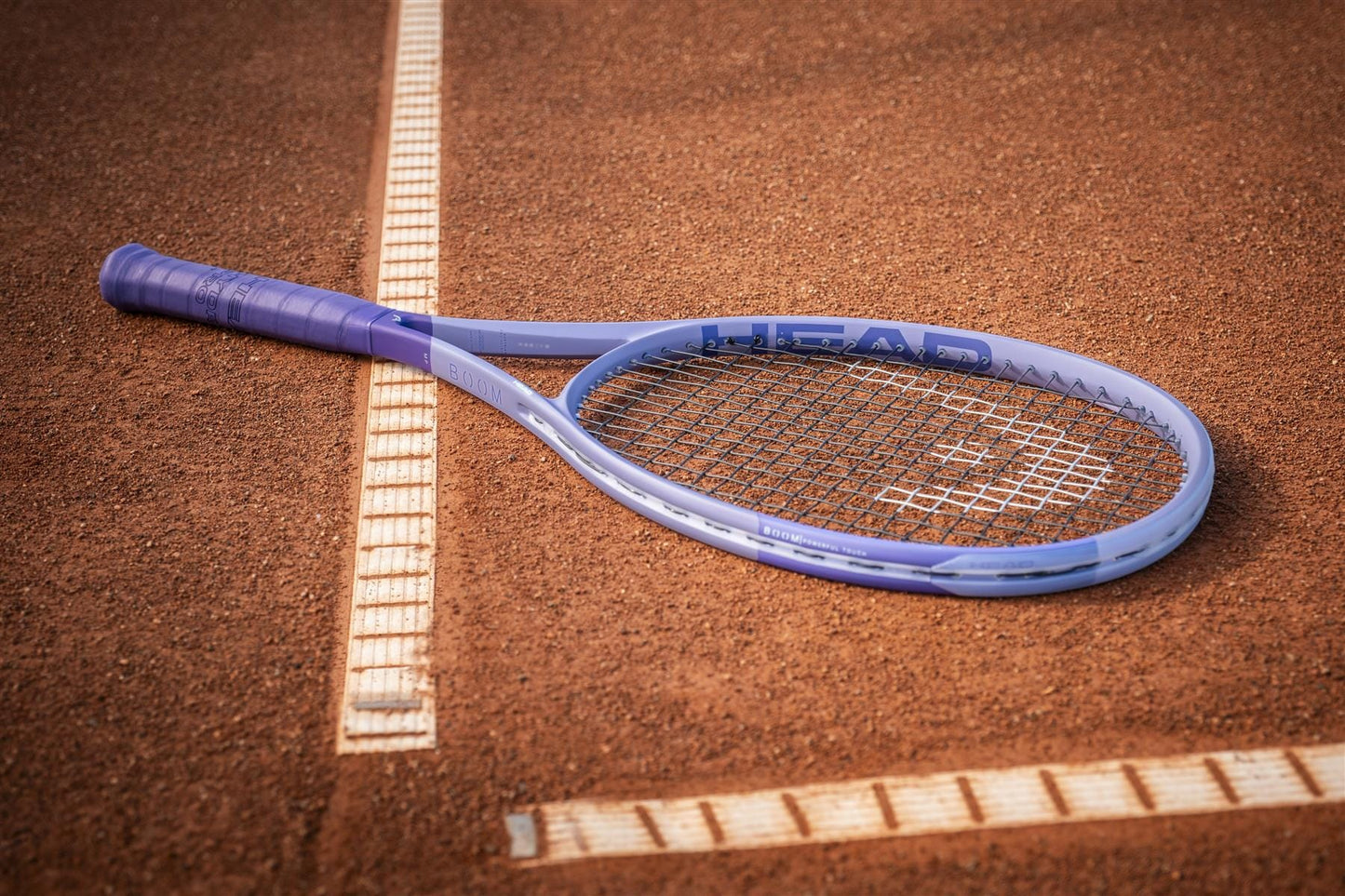 A HEAD Boom MP Alternate 2026 Tennis Racket, renowned for its explosive power, rests on a clay tennis court across the white boundary line.
