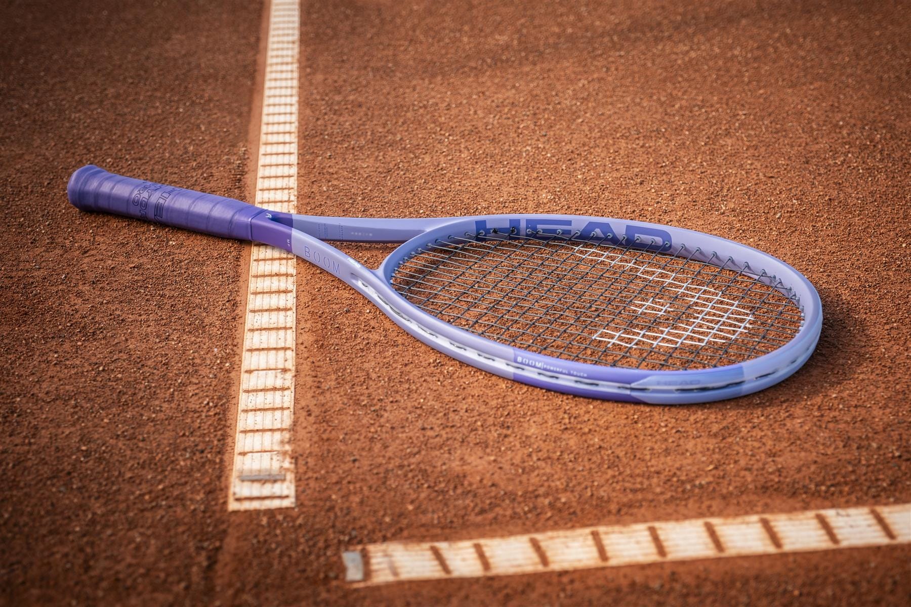 A HEAD Boom MP Alternate 2026 Tennis Racket, renowned for its explosive power, rests on a clay tennis court across the white boundary line.