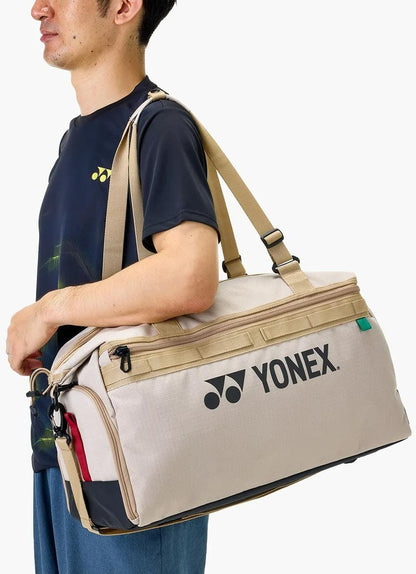 A person in a dark shirt carries the Yonex BA72611EX Gearlogic Tennis Boston Bag - Beige over their shoulder, standing against a plain white background.