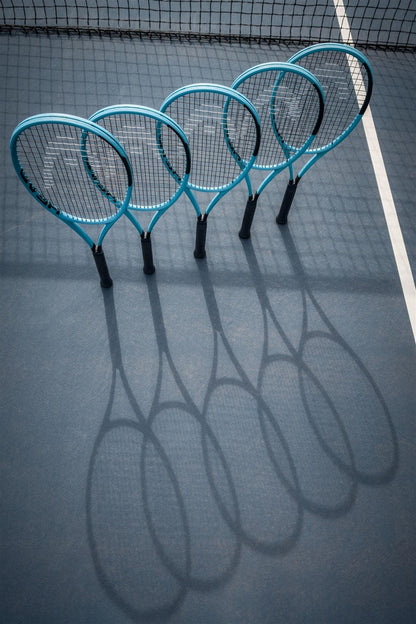 Four HEAD Boom Pro 2026 Tennis Rackets from HEAD stand upright on a tennis court near the net, casting clear shadows on the sunlit surface.