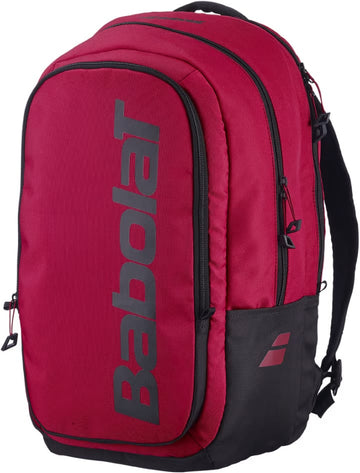 A Babolat Court Hero Tennis Backpack in Burgundy and Black is displayed at a three-quarter angle against a white background, showcasing a bold vertical Babolat logo on the front and multiple zippered compartments. Made from recycled polyester, this stylish tennis backpack is an eco-friendly option for athletes.
