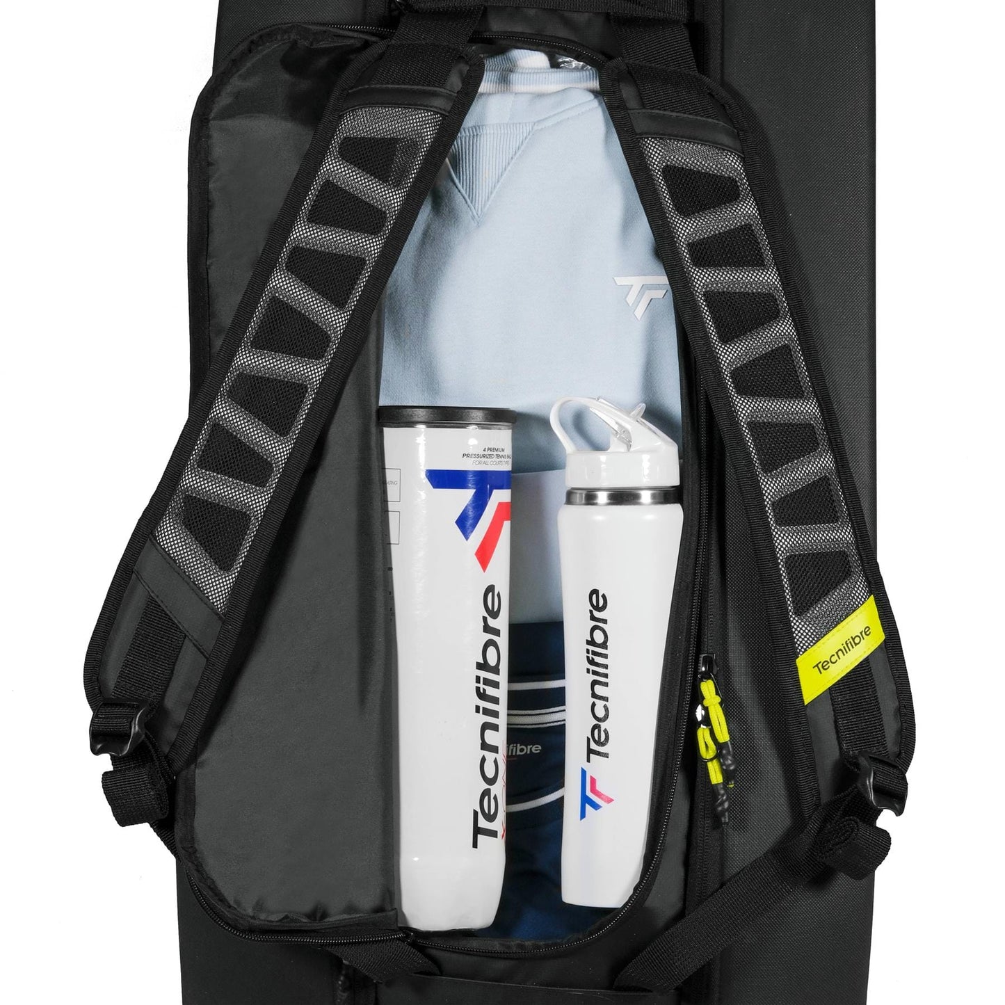 An open Tecnifibre Reform L Tennis Racket Bag in black shows a light blue shirt and two white Tecnifibre bottles with blue and red accents neatly packed inside.