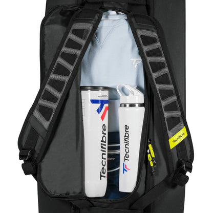 An open Tecnifibre Reform L Tennis Racket Bag in black shows a light blue shirt and two white Tecnifibre bottles with blue and red accents neatly packed inside.