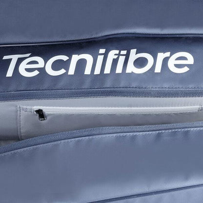 Close-up of a navy blue Tecnifibre Tour Endurance 2023 12 Racket Tennis Bag, showcasing the brand name in white letters. The focus is on a zippered compartment, partially unzipped, revealing a lighter gray interior crafted from durable tarpaulin material.