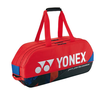 The Yonex 92431WEX Pro Tournament 6 Racket Tennis Bag in Scarlet is perfect for the professional tournament scene, featuring black and blue accents. This sports duffle bag offers two carrying straps, a padded handle, and dedicated compartments for rackets, with the Yonex logo prominently displayed.