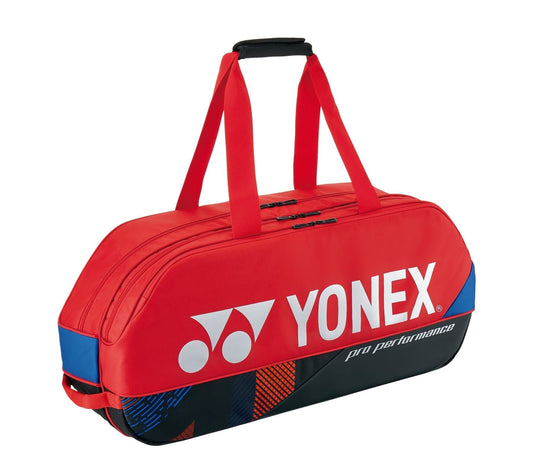The Yonex 92431WEX Pro Tournament 6 Racket Tennis Bag in Scarlet is perfect for the professional tournament scene, featuring black and blue accents. This sports duffle bag offers two carrying straps, a padded handle, and dedicated compartments for rackets, with the Yonex logo prominently displayed.