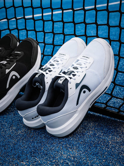 A pair of white sneakers and HEAD Revolt Court 5.0 Men's Tennis Shoes in White/Blueberry rest against a black tennis net on a blue court, highlighting HEAD’s stylish and comfortable footwear for every player.