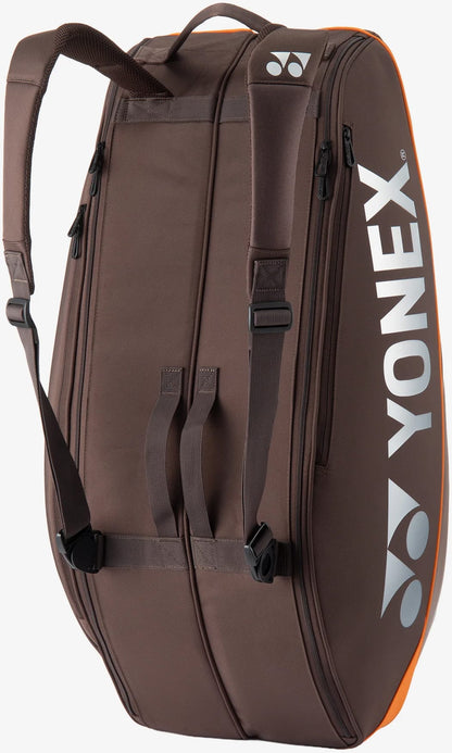 The Yonex 92426EX 6 Racket Pro Tennis Bag in Espresso Brown features shoulder straps, a side handle, and a prominent white Yonex logo. It includes orange accents, visible zippers, and is designed as a spacious bag for carrying up to six rackets or other sports equipment.