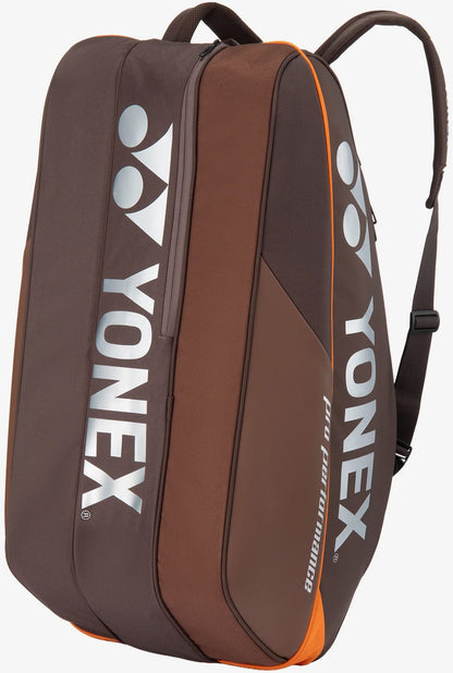 The Yonex 92429EX 9 Racket Pro Tennis Bag in Espresso Brown features two shoulder straps, prominent white Yonex logos, and orange accents. Designed to securely and conveniently carry tennis equipment, this bag offers multiple compartments and can hold up to nine rackets.