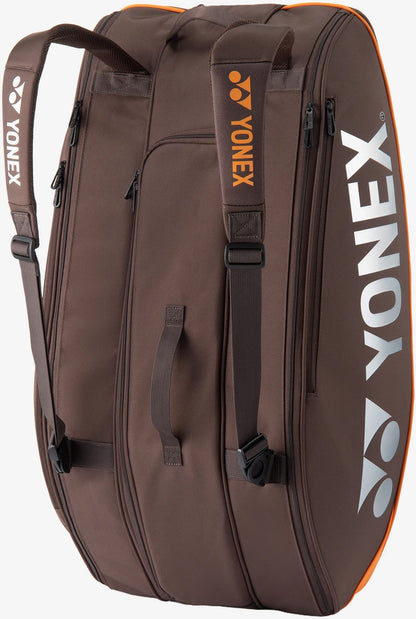 The Yonex 92429EX 9 Racket Pro Tennis Bag in Espresso Brown features striking orange accents, comfortable shoulder straps, and multiple zippered compartments. Designed for serious players, this spacious bag can hold up to nine rackets and prominently displays the Yonex logo in white on both the side and the strap.