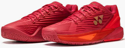 Yonex Power Cushion Eclipsion 5 Men's Tennis Shoes in Ruby Red feature textured patterns, red laces, gold Yonex logos, an orange-accented midsole with advanced Power Cushion tech, and a herringbone outsole for superior grip.