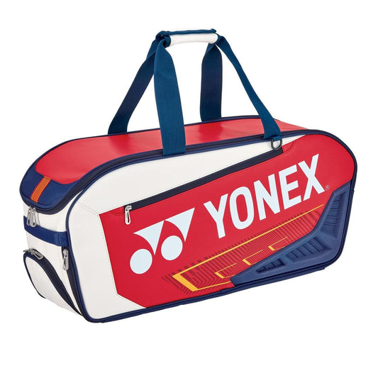 The Yonex 02331WEX Expert Tournament Tennis Bag is a chic duffel showcasing a white, navy, and red palette. Adorned with a prominent Yonex logo, it boasts sturdy handles and several zippered compartments, including a handy shoe pocket. This bag is ideal for transporting your sports gear in tournament style.