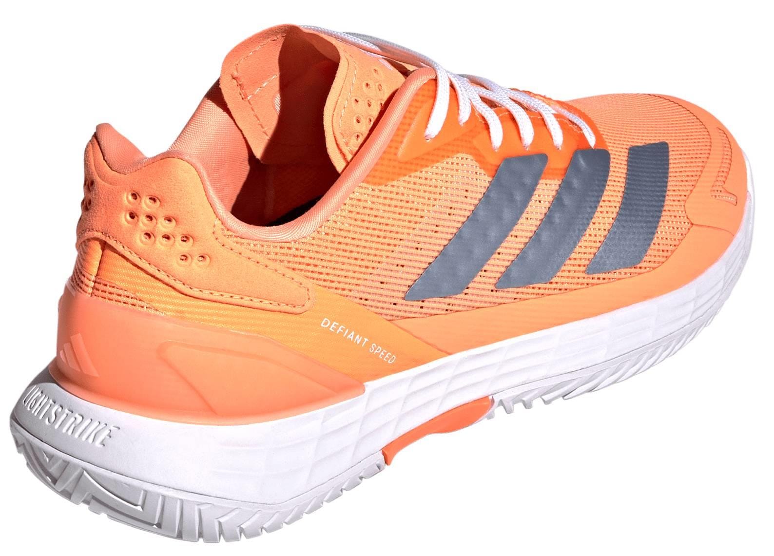 The adidas ADIDAS Defiant Speed 2 Womens Tennis Shoes in orange feature white laces, a white sole, three gray side stripes, "Defiant Speed" text, and textured heel and sole details for lightweight performance.