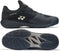 A pair of Yonex Power Cushion Sonicage Men's Tennis Shoes in Black/Mocha Grey is shown from the side and bottom, featuring the Yonex logo, mesh details, and a zigzag textured sole for lightweight comfort.
