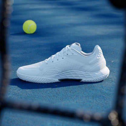 An adidas Defiant Speed 2 Men's Tennis Shoe in Cloud White, Core Black, and Grey rests on a blue court, a yellow tennis ball behind it. A blurred racket frames this sleek lightweight style from adidas.