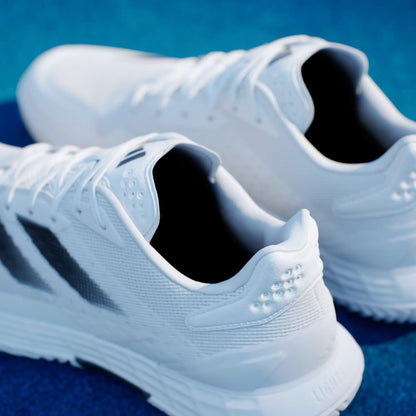 A close-up of adidas Defiant Speed 2 Men's Tennis Shoes in Cloud White, Core Black, and Grey on a blue surface, showing the mesh texture, laces, and heel design of this lightweight speed tennis shoe.