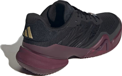 An adidas Barricade 14 Men’s Tennis Shoe in Core Black and Maroon, accented with gold and three signature black side stripes, is shown from the back left angle. Designed for baseline players who want both style and performance, it features a textured sole for optimal grip.
