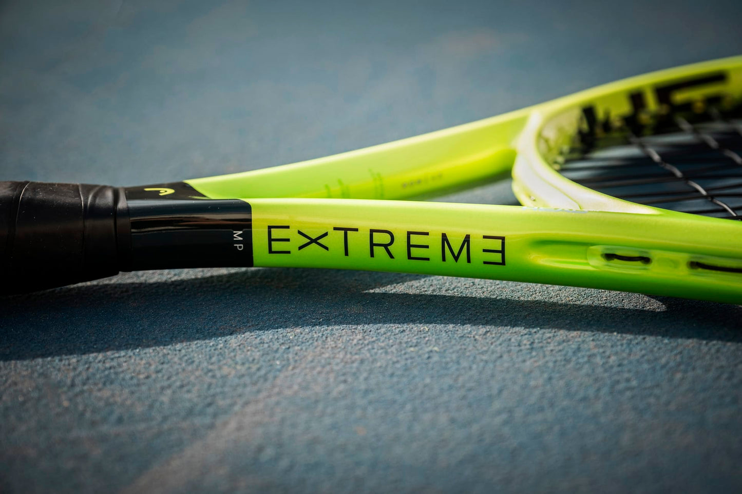 A close-up of the HEAD Extreme MP 2026 Tennis Racket in vibrant yellow-green rests on a court surface, featuring the word "EXTREME" printed near the handle on the frame and showcasing HEAD's signature design focused on power and spin.
