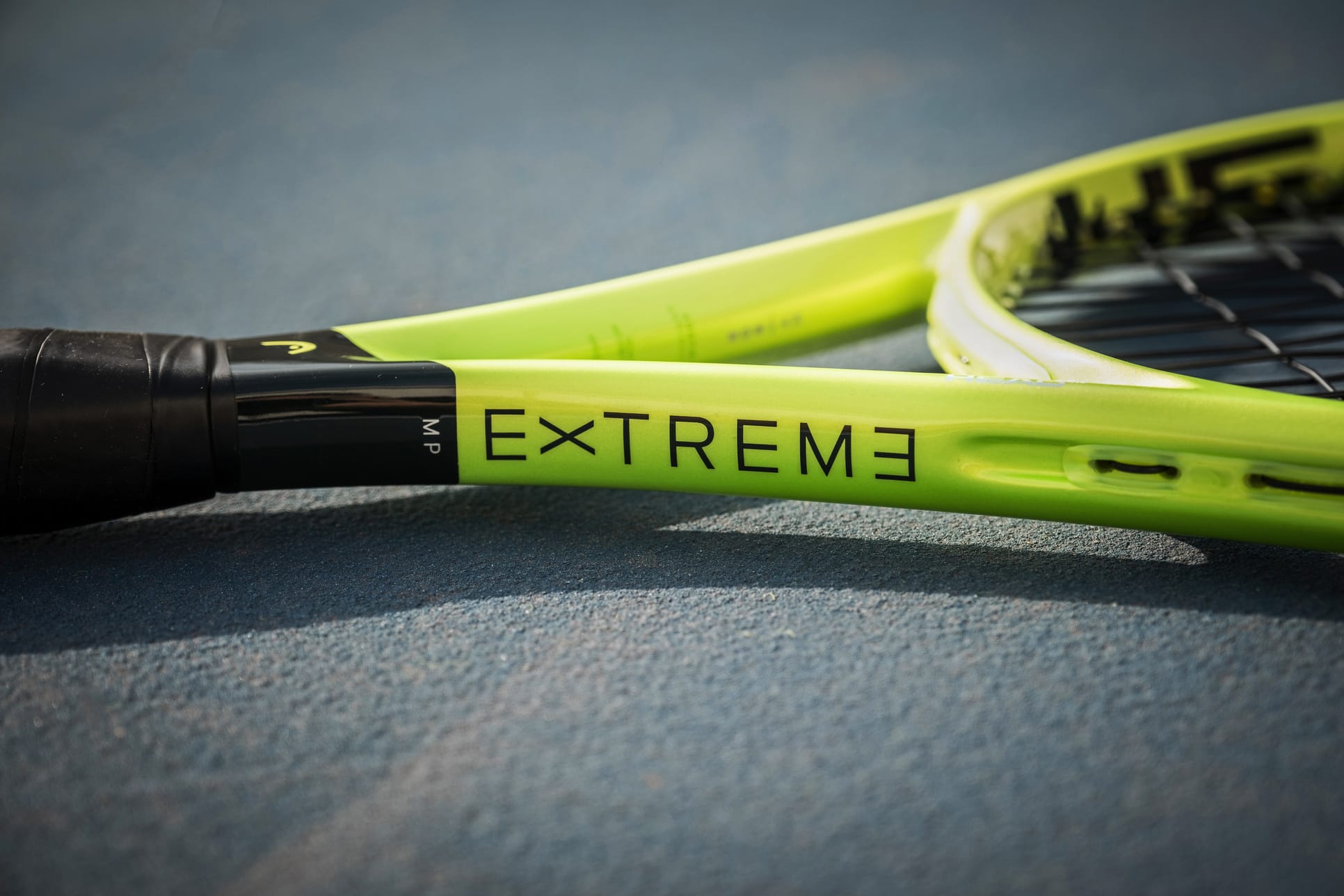A close-up of the HEAD Extreme MP 2026 Tennis Racket in vibrant yellow-green rests on a court surface, featuring the word "EXTREME" printed near the handle on the frame and showcasing HEAD's signature design focused on power and spin.