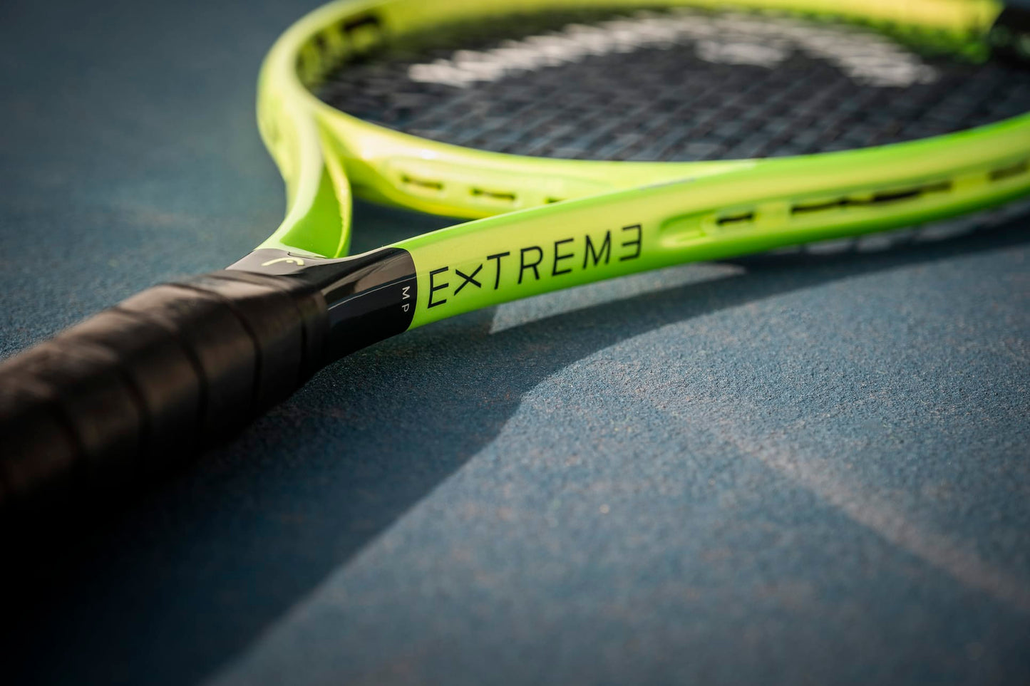 A close-up of the HEAD Extreme MP 2026 Tennis Racket by HEAD, featuring the "EXTREME" label, rests on a blue tennis court and showcases its handle and frame engineered for enhanced power and spin.